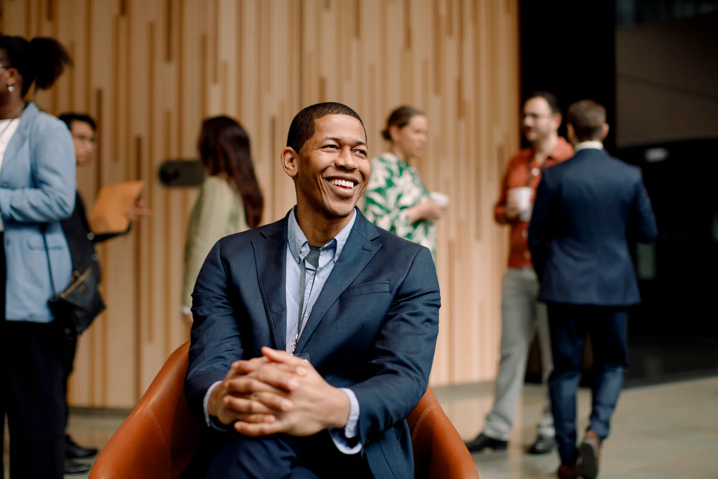 Portrayal of Capella student seated in a leather chair with coworkers in background.