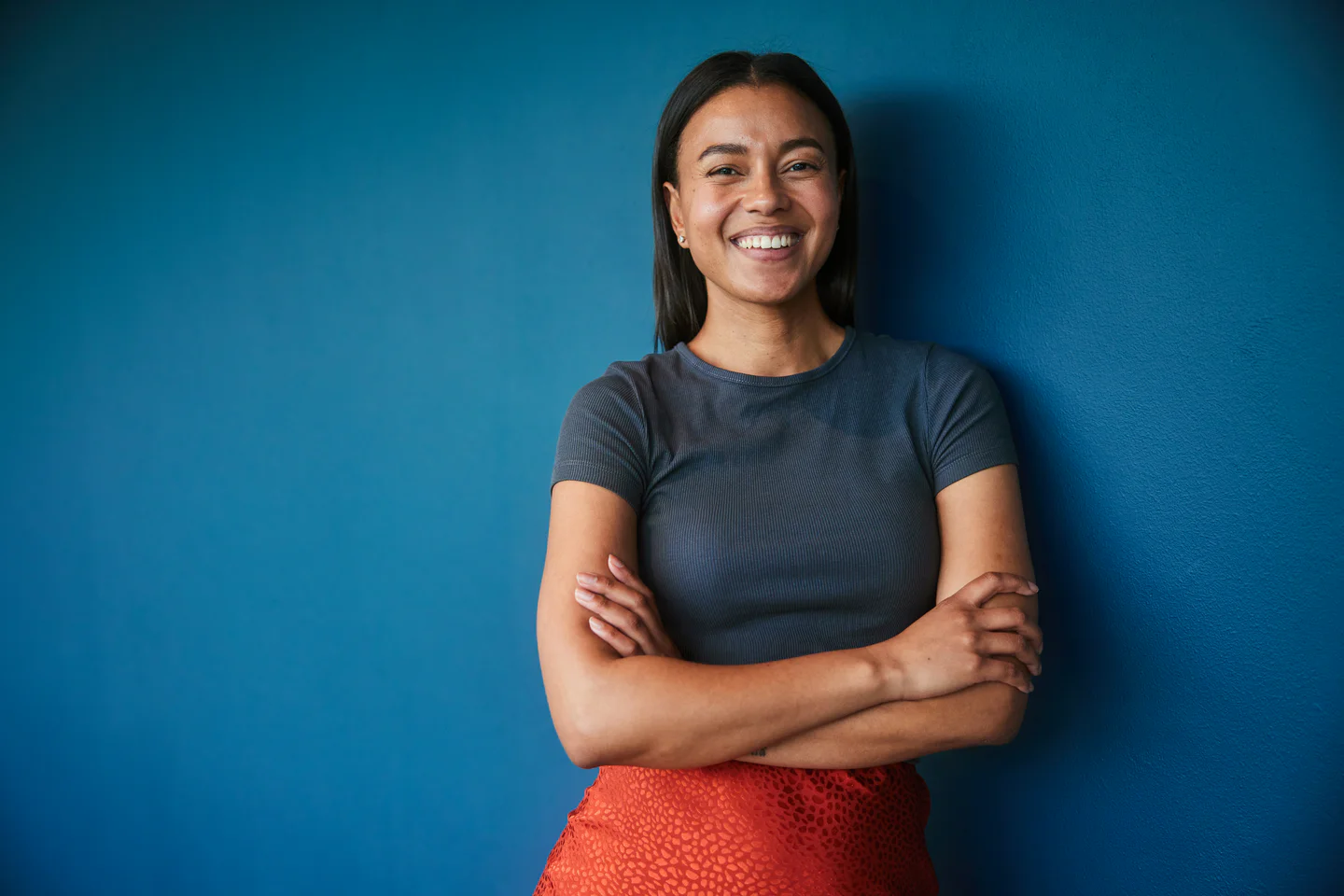 Portrayal of confident, smiling Capella alum with arms folded and standing a blue wall.