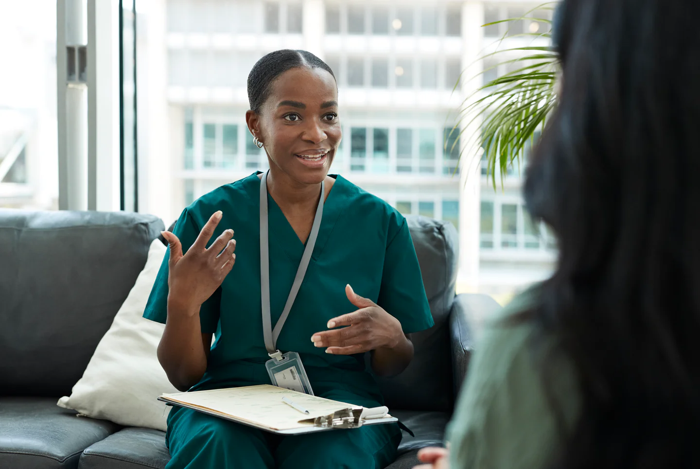Portrayal of a Capella University online nursing student in scrubs&nbsp;holding a clipboard and talking to a patient.