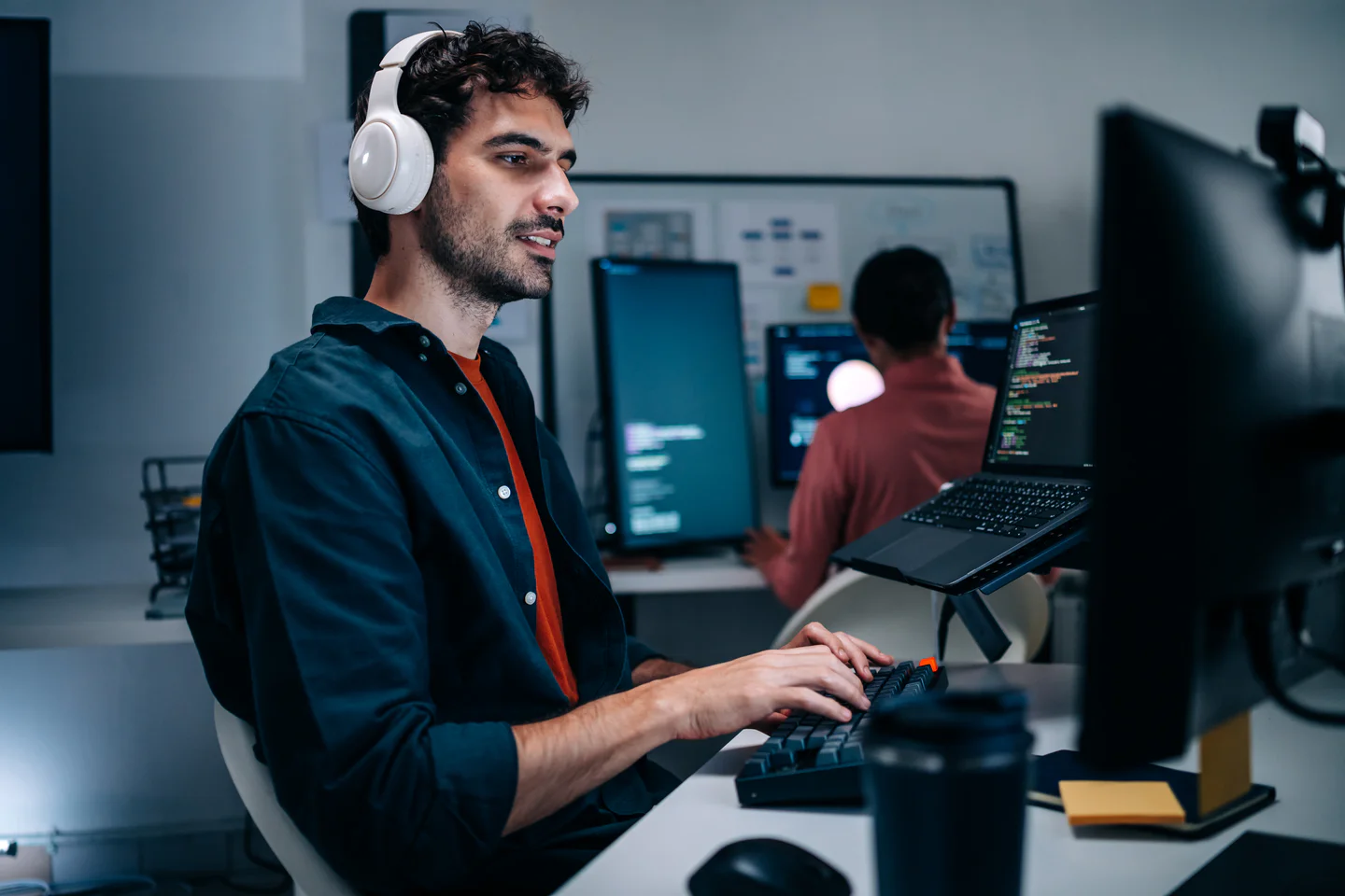 Portrayal of Capella IT student wearing headphones while doing work at several monitors.