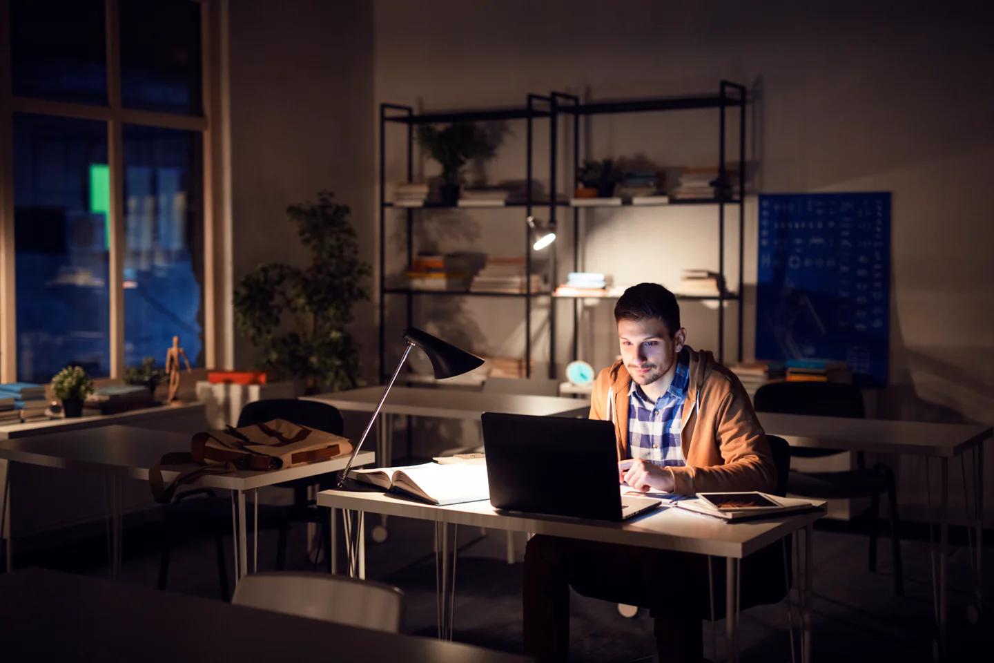 Portrayal of a Capella student studying on a laptop at night in their home office.