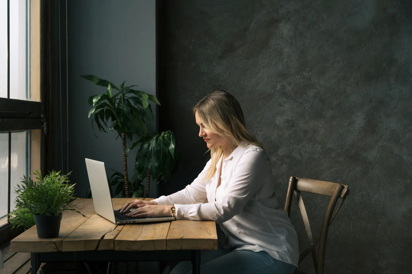 Portrayal of a Capella student typing on their laptop at a wooden desk with plants.