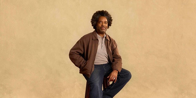 man with afro wearing brown jacket sitting on a stool