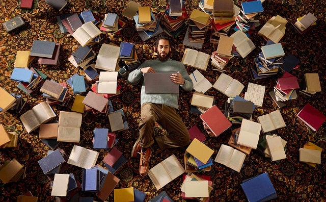 man laying on ground next to a large pile of books