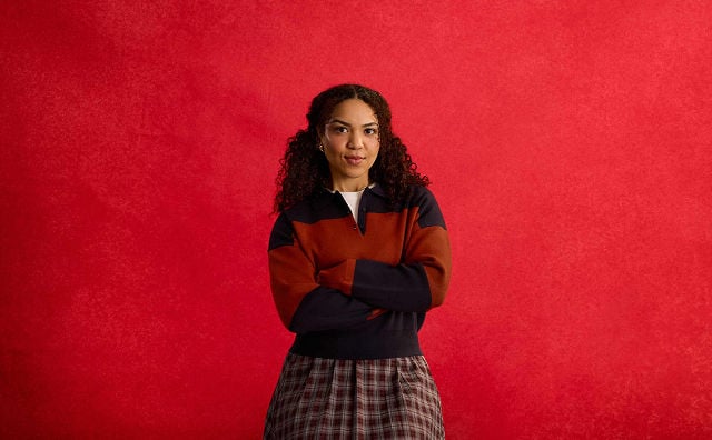 woman wearing a red and blue sweater and maroon skirt with her arms crossed standing confidently