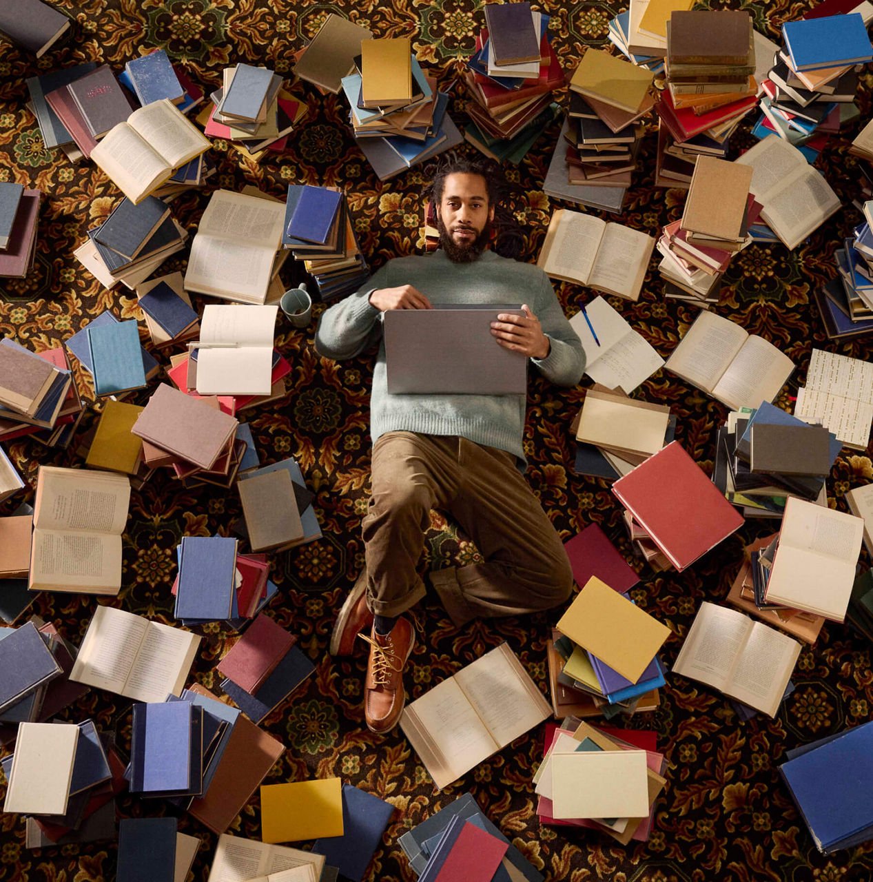 man laying on ground next to a large pile of books