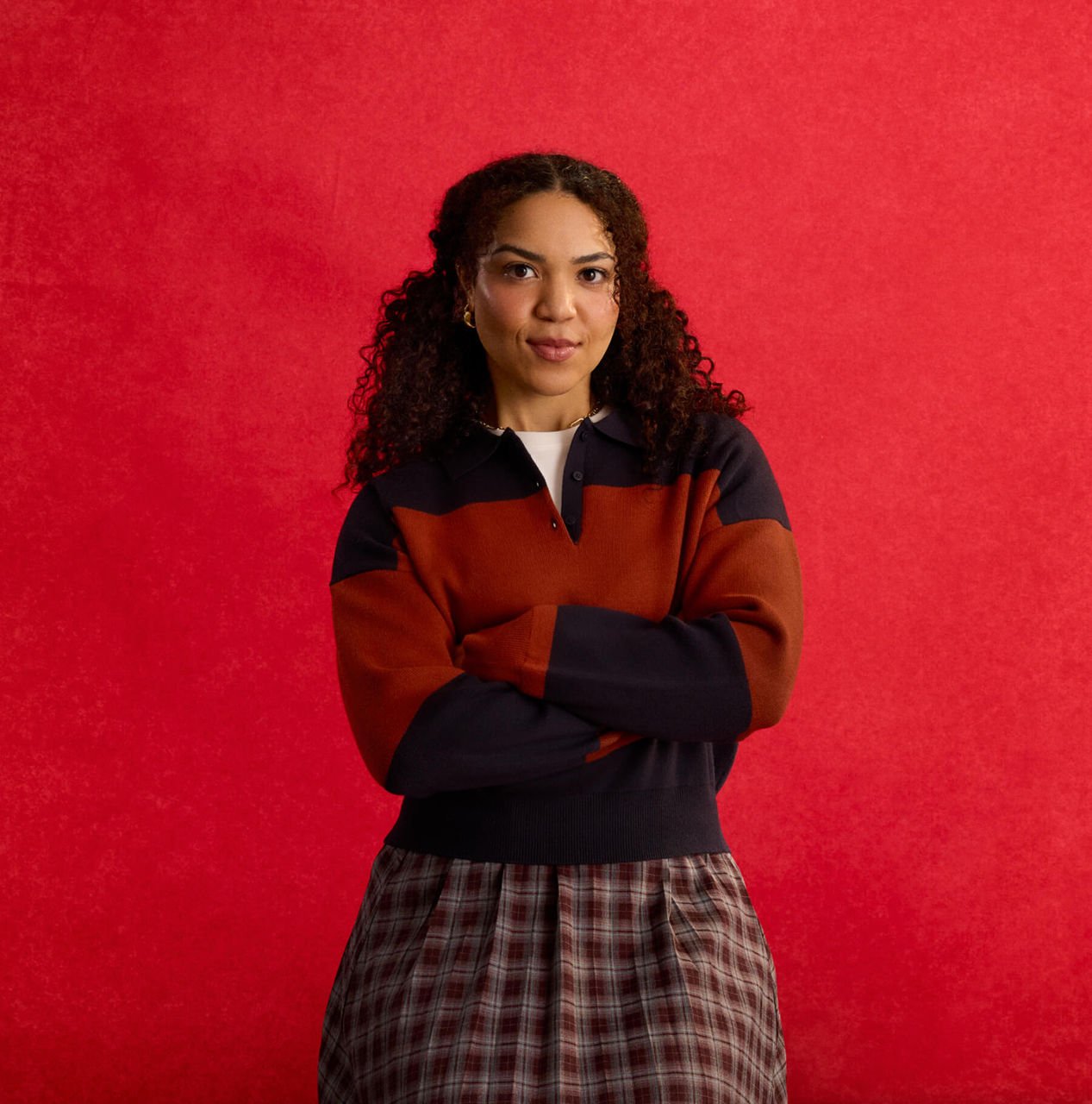 woman wearing a red and blue sweater and maroon skirt with her arms crossed standing confidently