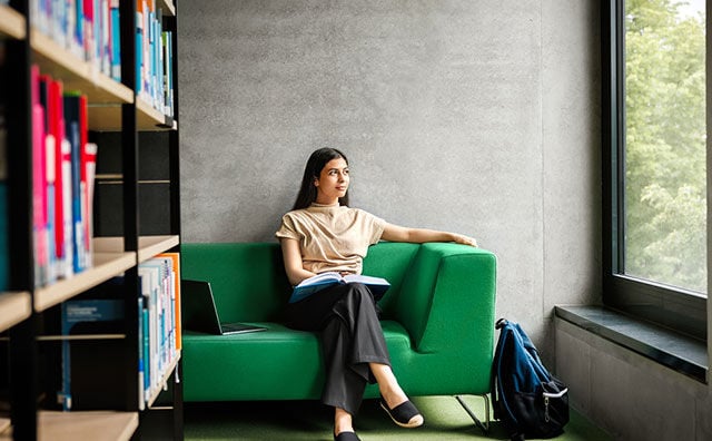 woman sitting on large green sofa with a book
