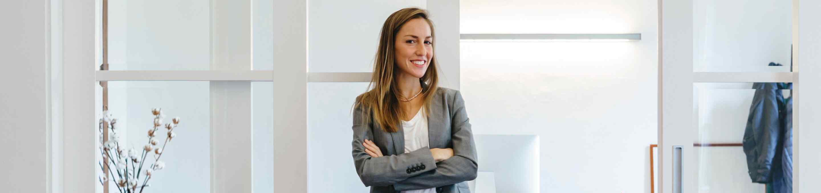 blonde woman wearing a grey blazer smiling with her arms crossed