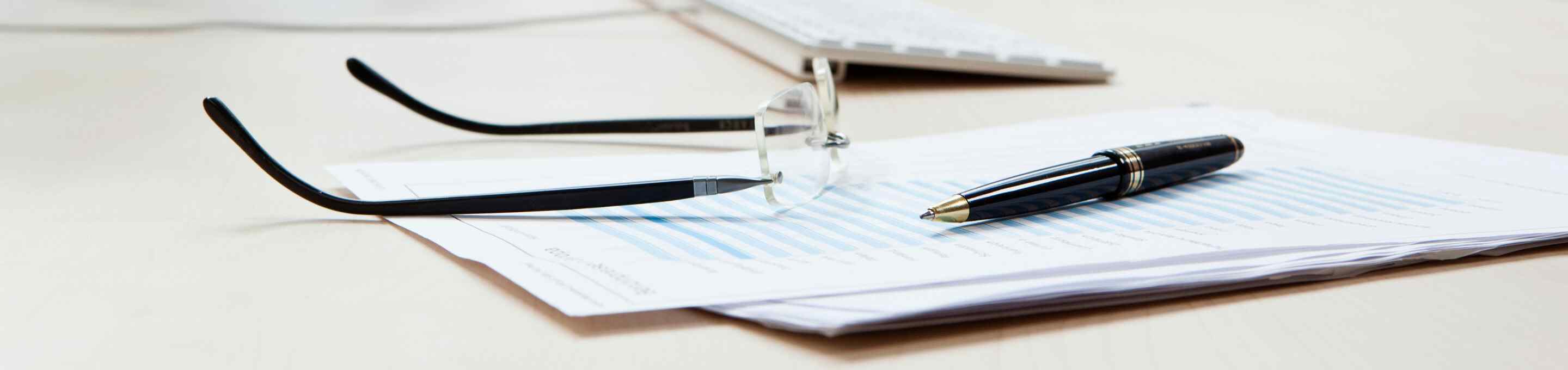 pair of glasses and a pen on a notepad on a desk