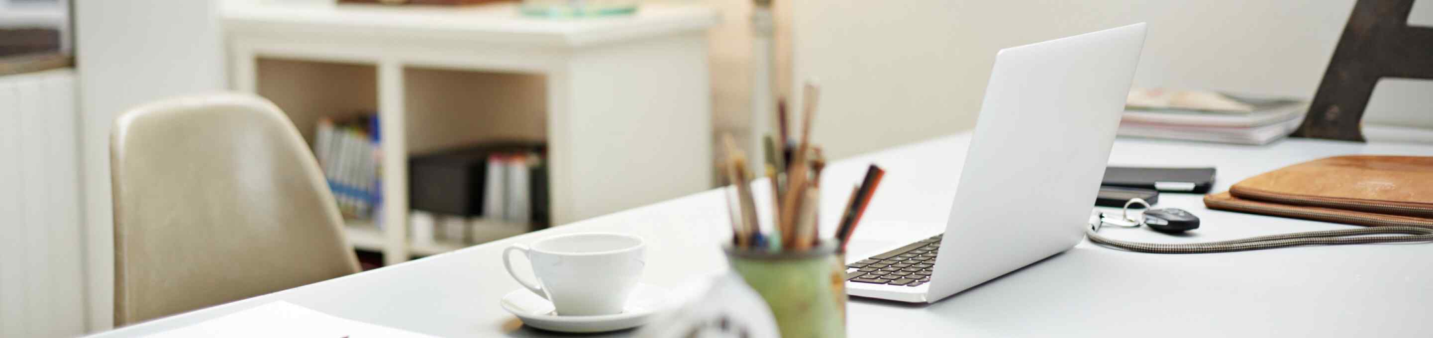 White teacup and laptop on a white desk in a home office