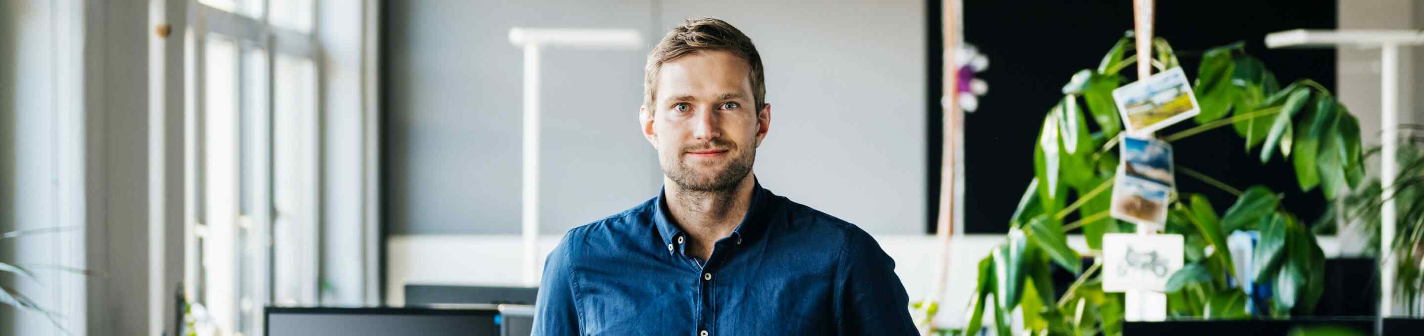 man in blue shirt staring at camera with plants and office in the background
