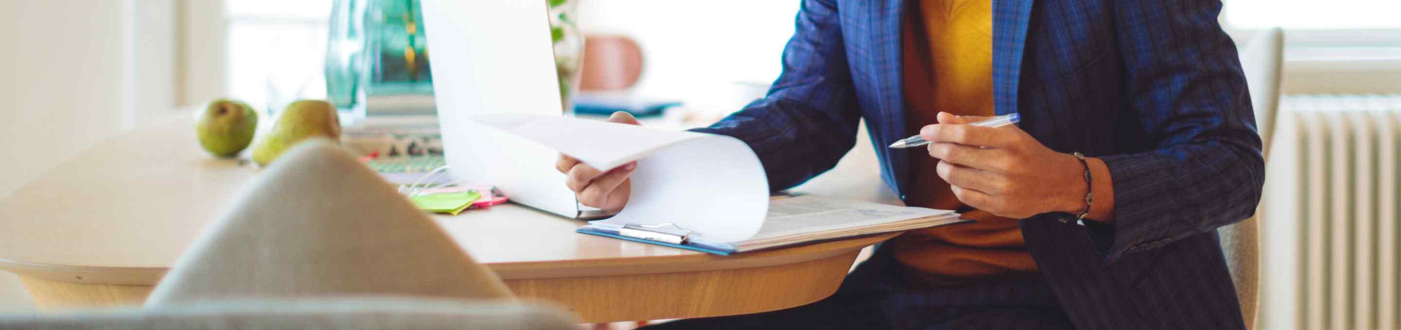 Man in blue striped suit and yellow sweater looking at a clipboard