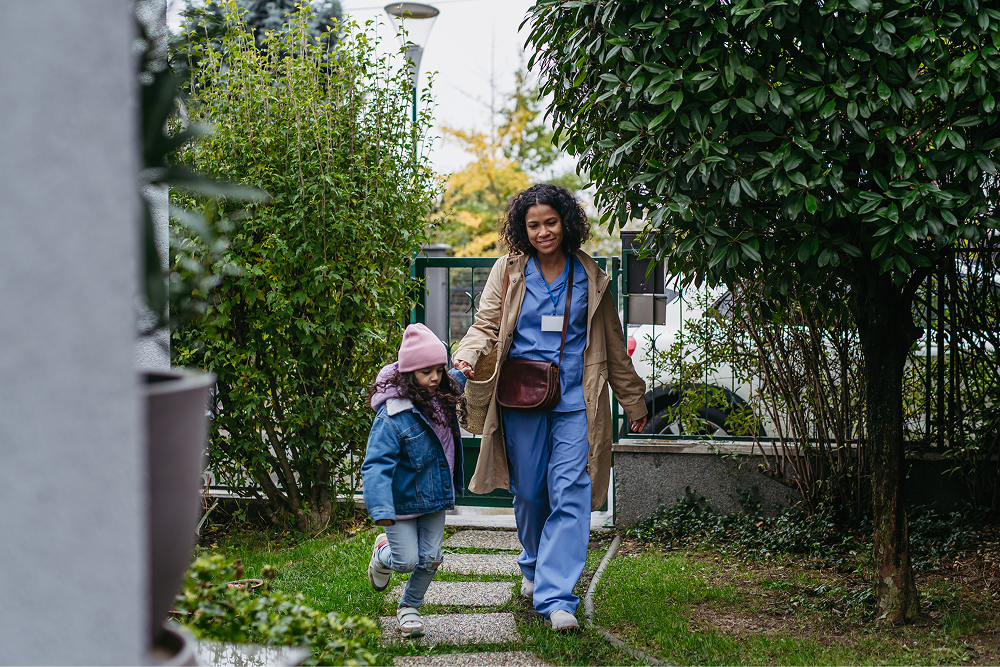 Portrayal of Capella University student in scrubs walking on an outdoor path with her child.