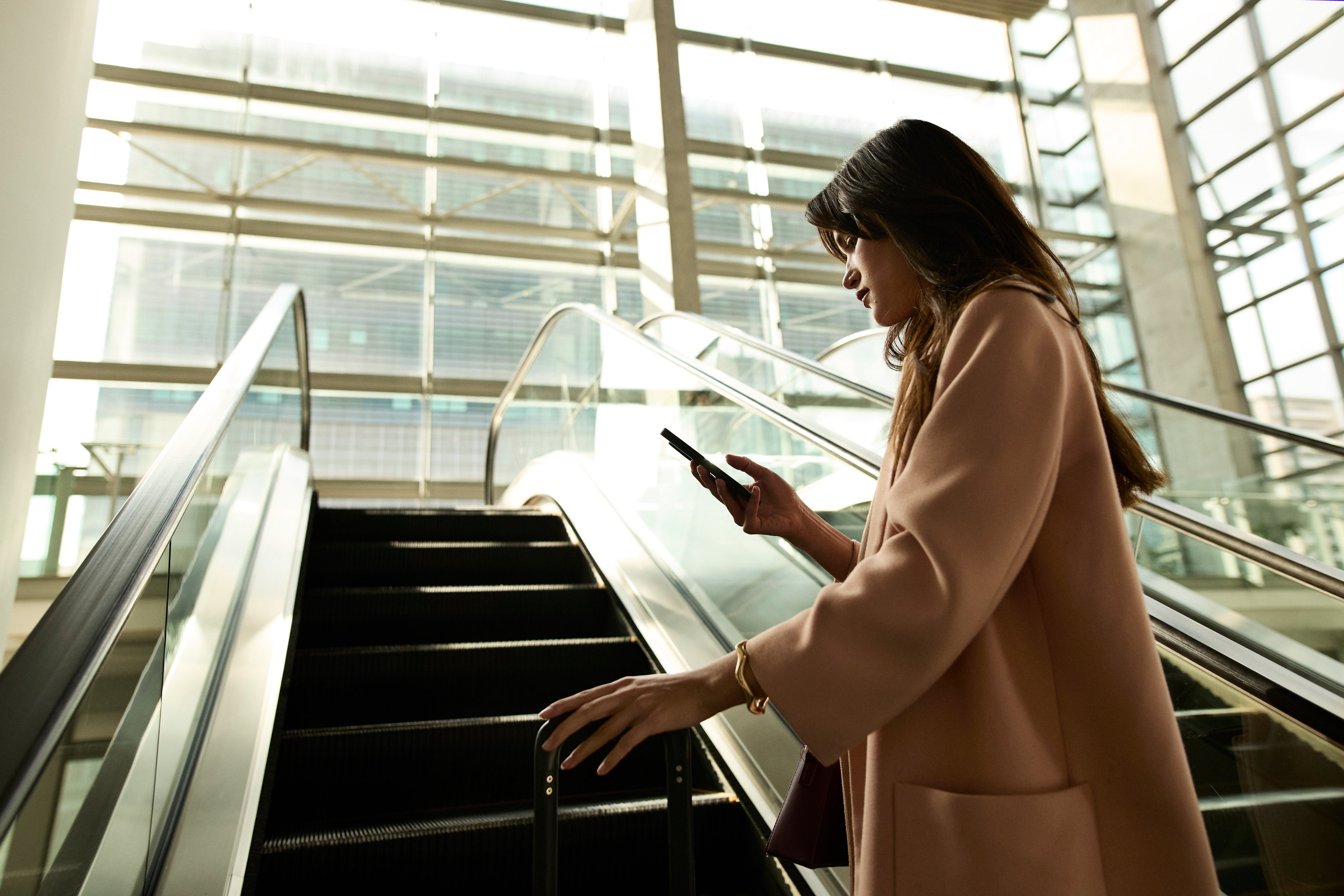Portrayal of a Capella University online MBA student looking at her cell phone while on an escalator.