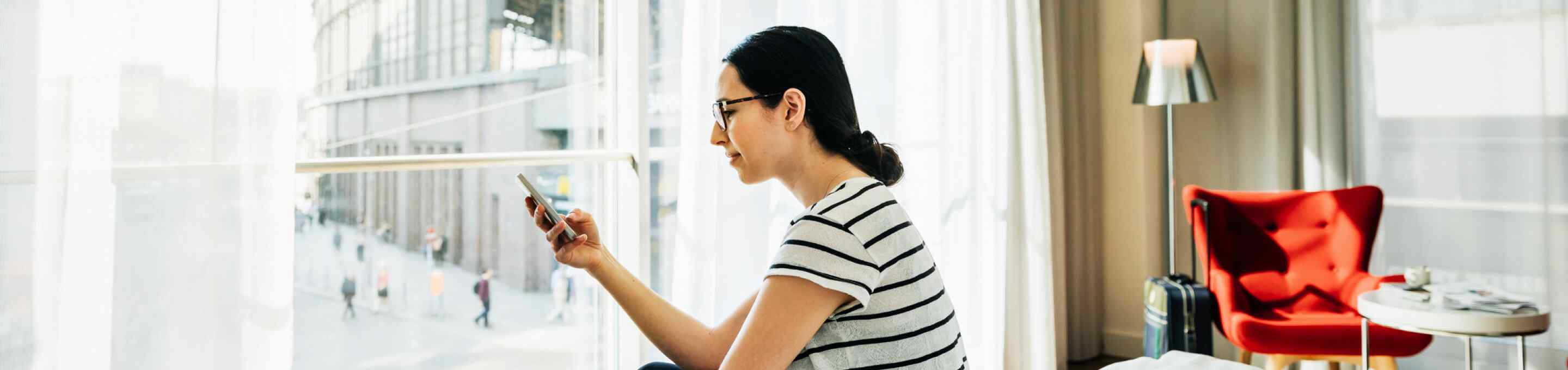 woman in a striped shirt laying on a bed using a smartphone