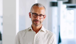 Professional man in a white shirt and glasses in a modern office setting with soft lighting.