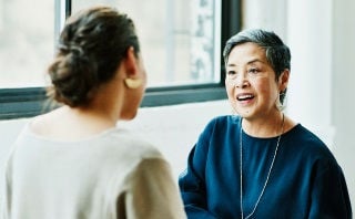 Two women having a friendly conversation near a window.